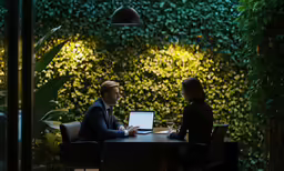 two people sitting at a table working on a laptop