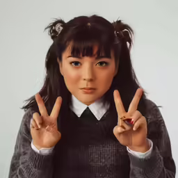 young asian girl giving a peace sign and wearing a sweater