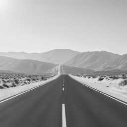 a long empty road surrounded by mountains on a clear day
