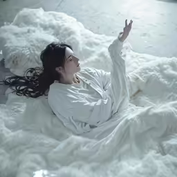a girl laying on a bed with white sheets