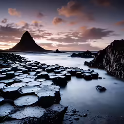 a rocky beach next to a mountain under cloudy skies