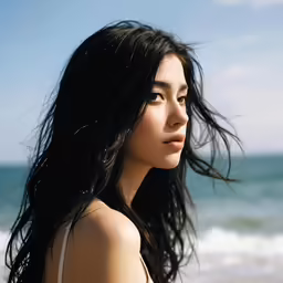 an asian woman with long hair standing in front of the ocean