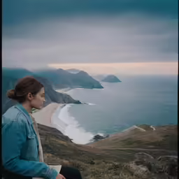 a woman is sitting on a cliff overlooking the water