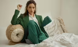 a woman sitting on the bed wearing green clothing