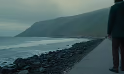 a man stands alone on a paved path overlooking a body of water