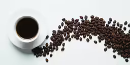 a cup of coffee and some coffee beans on a white surface