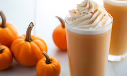 orange drink with whipped cream on top next to two pumpkins