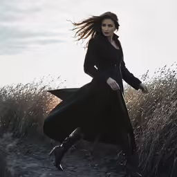 woman in a long coat running through the grass