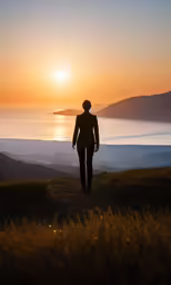 a woman stands alone on top of a hill, watching the sunset