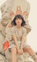 a girl sits in front of a rock statue