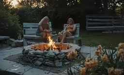 two women sitting by a fire pit on bench