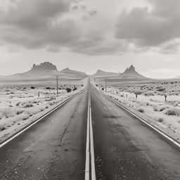 black and white photograph of an empty highway with mountains in the distance