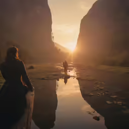 two people are walking through a small creek as the sun sets