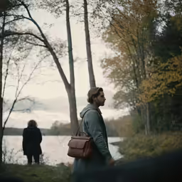 the man carries a brown leather bag beside the river