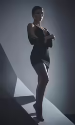 a woman poses in a black bodysuit against a gray background
