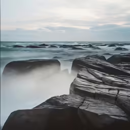 waves splash over rocks on the beach during a sunny day