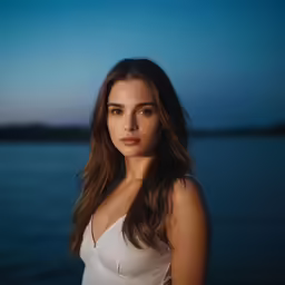 a woman in a white dress posing in front of a lake at sunset