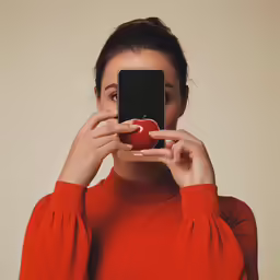 a woman in a red shirt holding an apple and looking at her phone