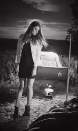 black and white photo of woman standing next to abandoned car