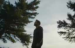 a man is standing in front of trees and looking to the sky