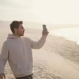 man taking photo with cellphone on the beach