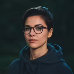 a woman with glasses standing in front of trees
