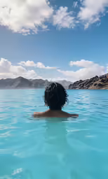 person swimming in blue lake with mountains in background