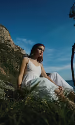 woman with long white dress sitting on rock near ocean