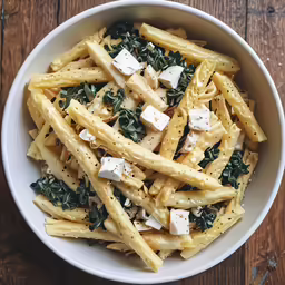 pasta with spinach, cheese and white sauce in a white bowl