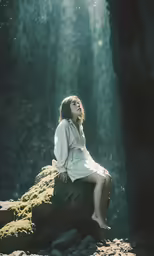 the woman sits on a rock with the sun coming through the trees