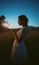 woman in white dress standing in grassy field at sundown