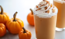 three pumpkin drinks sit beside small orange pumpkins