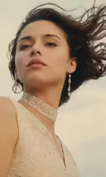 the beautiful woman wearing large earrings stands in front of a cloudy sky