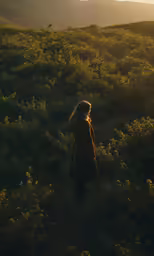 a woman stands on the top of a grassy hill