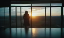 a woman standing in front of a window with the sun setting