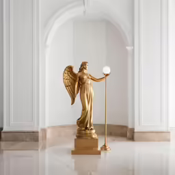 golden angel with white sphere standing on marble surface in large open space