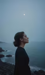 a woman standing by the ocean with an eclipse in the sky