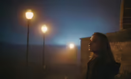 a woman standing under street light in a foggy night
