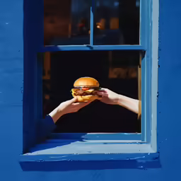 a hand holding a burger is reaching out of the window