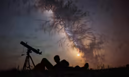people laying down under a tree while using telescopes