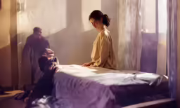 a young woman sitting on top of a bed next to a person in a room