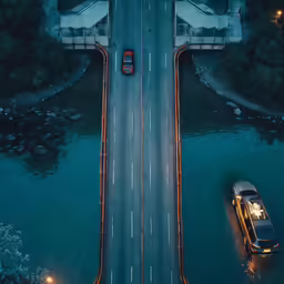 an overhead view of two cars on a road that goes over water