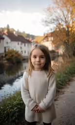 a little girl standing by the river in the fall