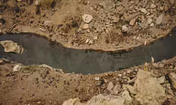 a hole in the ground near rocks and water