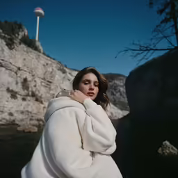 the woman is wearing a coat near a body of water