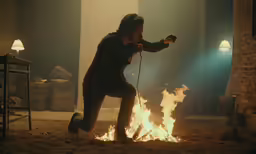 a man squats next to a bonfire