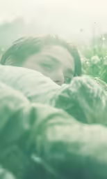 woman in grass laying down with blanket wrapped around her neck