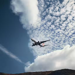 an airplane flying low in the sky near a hill