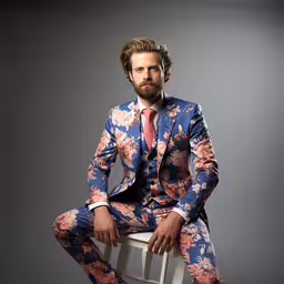 a man sitting on a stool wearing a colorful suit,a man in a floral suit sitting on a stool