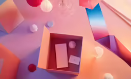 a pink and blue surface with a box, tissue paper balls, a glass chandelier and a red string